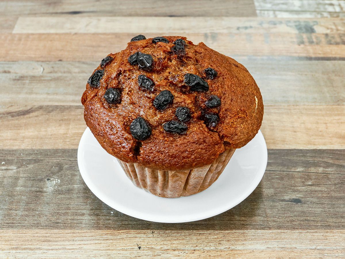 A muffin with blueberries on a white plate on a wooden table.