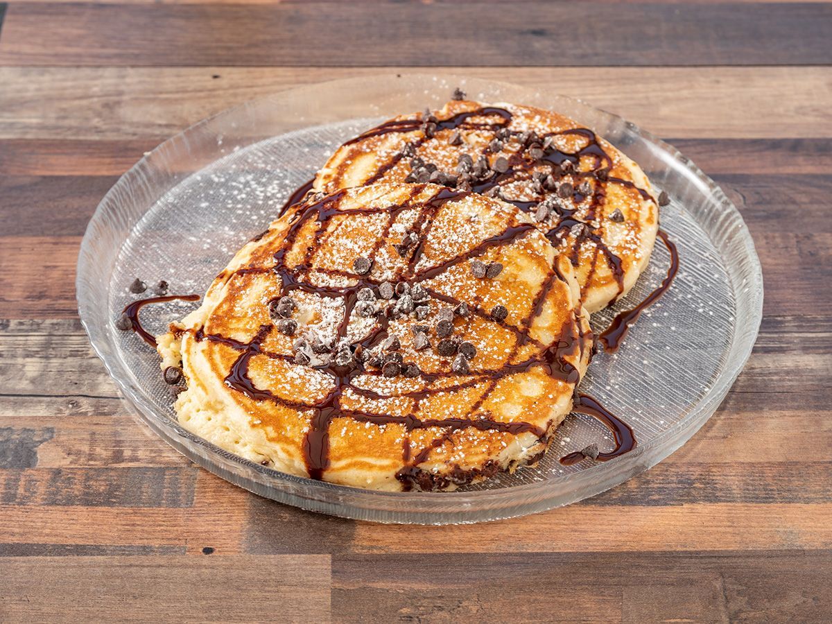 A plate of pancakes with chocolate sauce and powdered sugar on a wooden table.