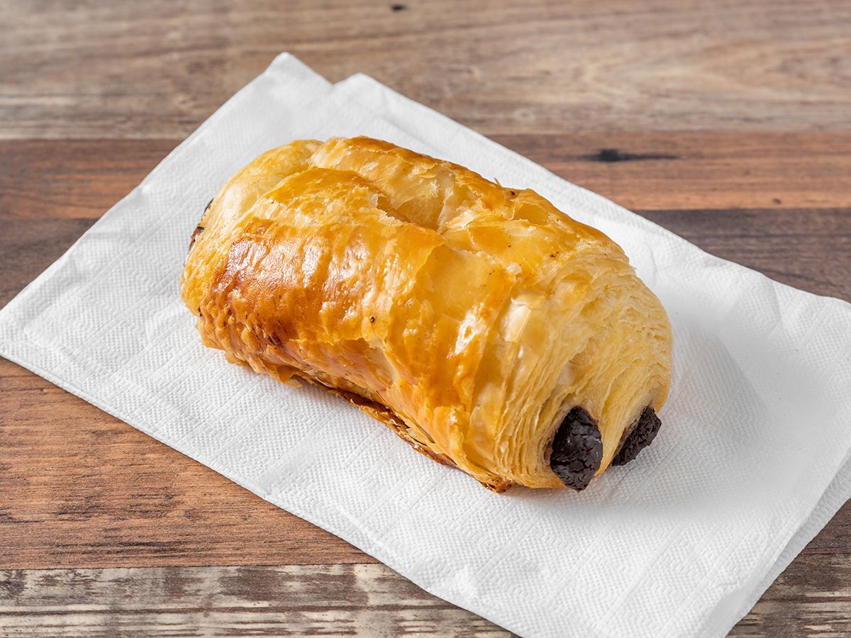 A chocolate croissant is sitting on a napkin on a wooden table.