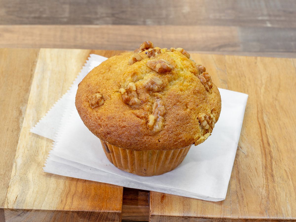 A muffin with walnuts on top is sitting on a napkin on a wooden table.