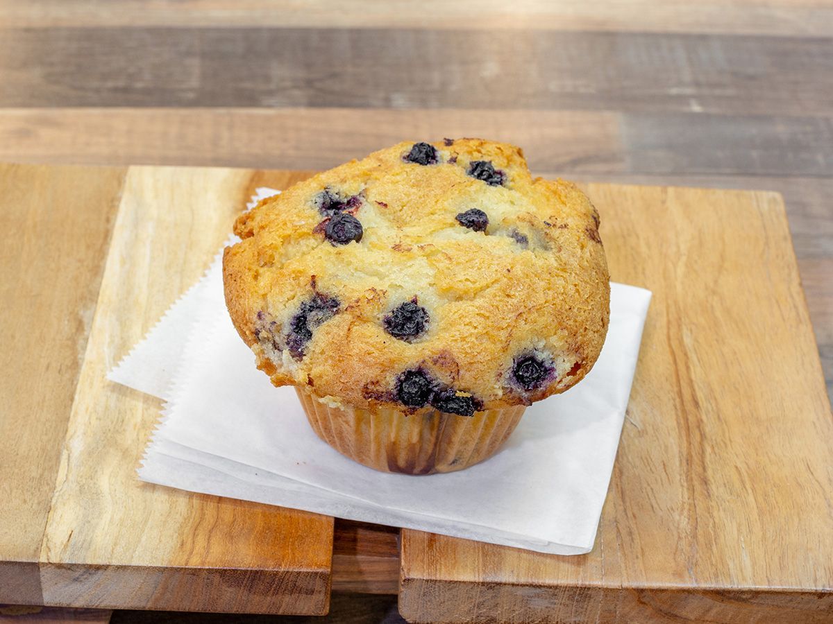 A blueberry muffin is sitting on a napkin on a wooden cutting board.