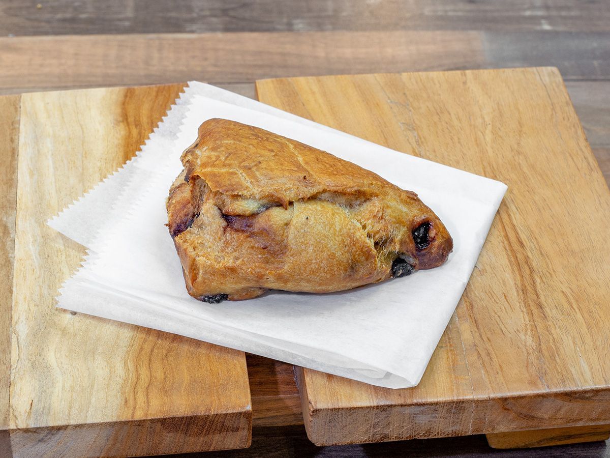 A blueberry scone is sitting on a napkin on a wooden cutting board.