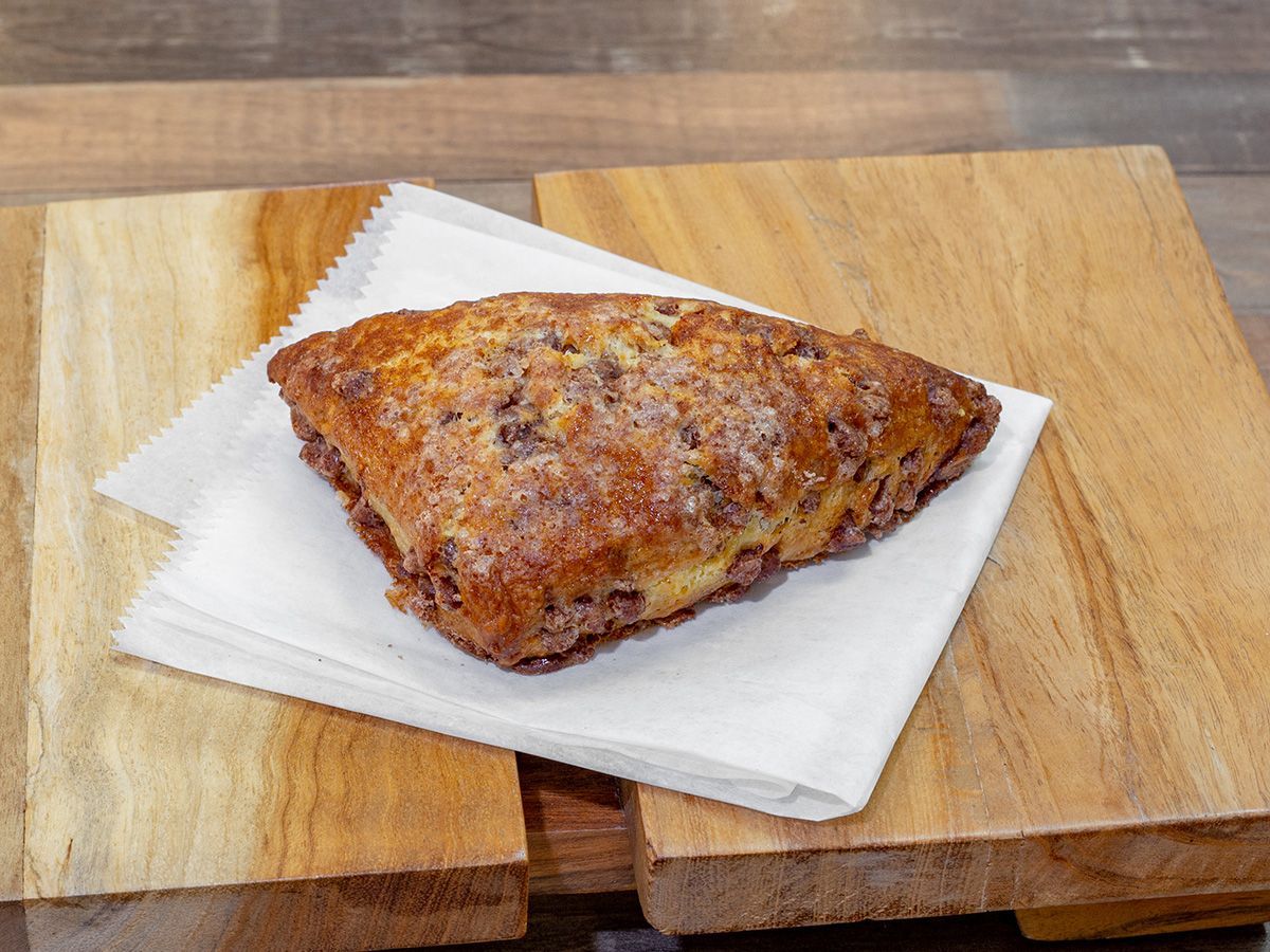 A scones is sitting on a napkin on a wooden cutting board.