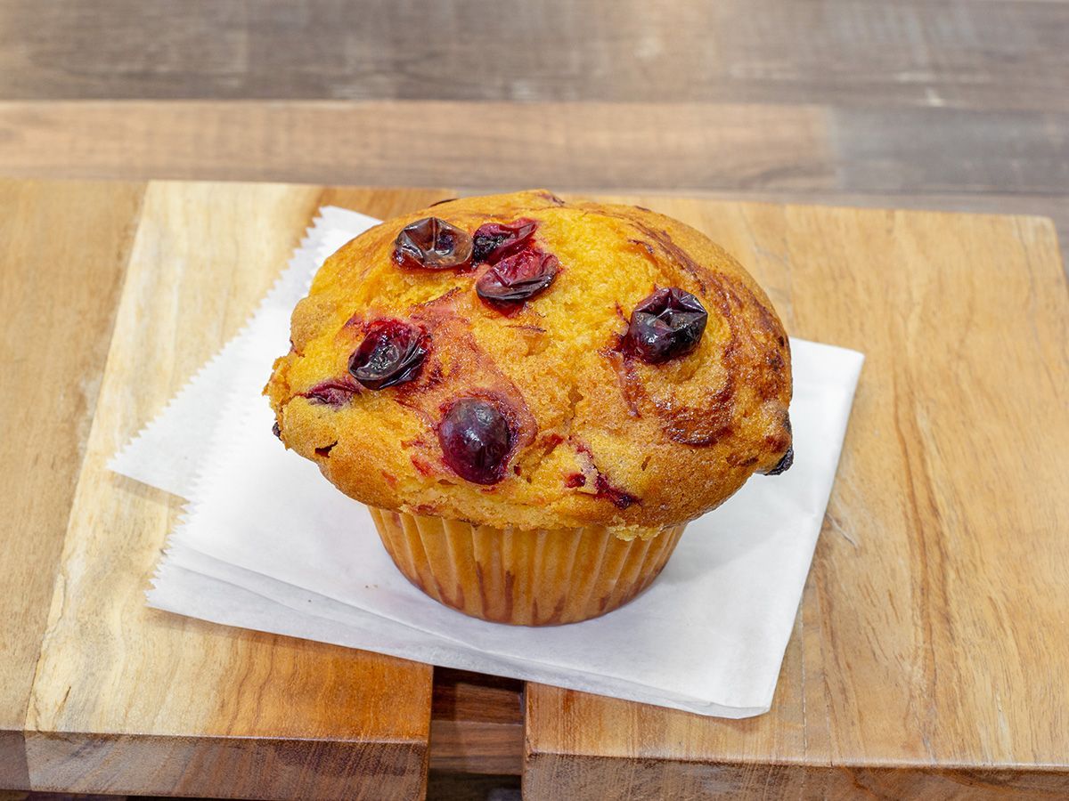 A muffin with cranberries on top is sitting on a napkin on a wooden table.