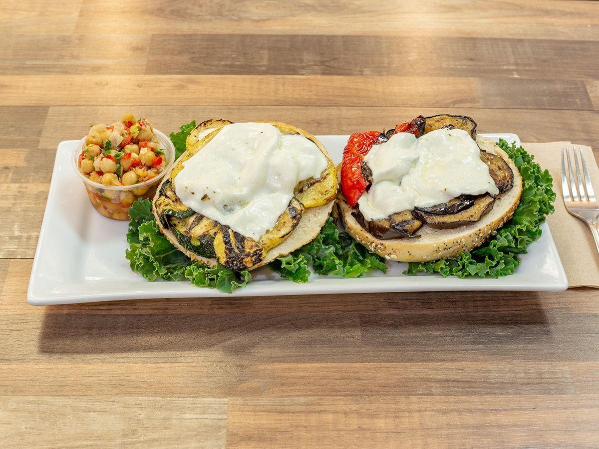 A white plate topped with two sandwiches and a side of chickpeas on a wooden table.