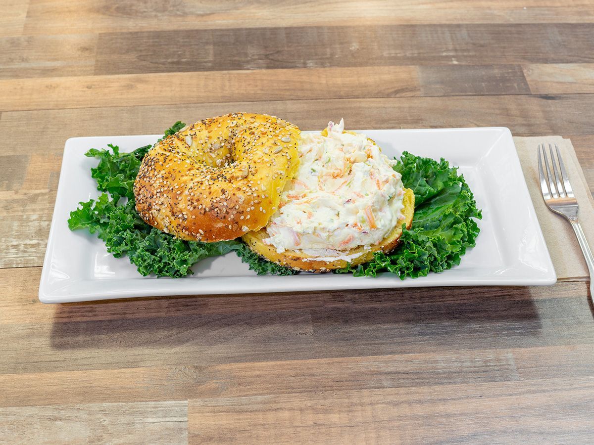 A bagel and coleslaw sandwich on a white plate on a wooden table.