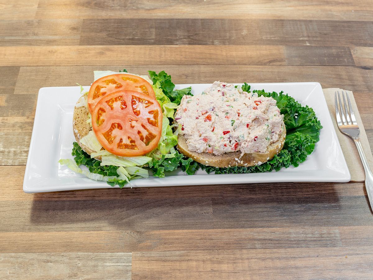 A crab salad sandwich on a bagel with lettuce and tomatoes on a white plate on a wooden table.