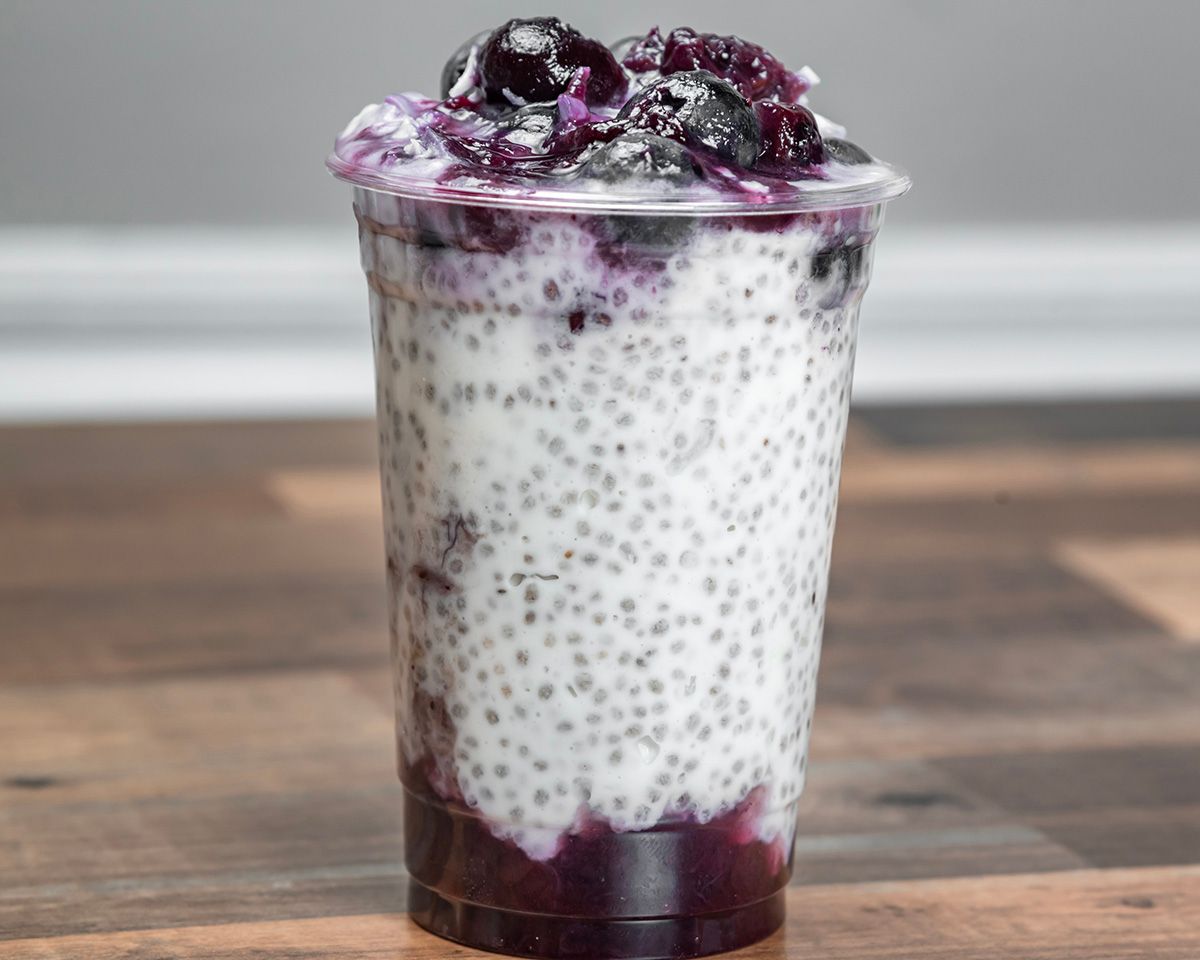 A cup of chia seed pudding with blueberries on top is sitting on a wooden table.