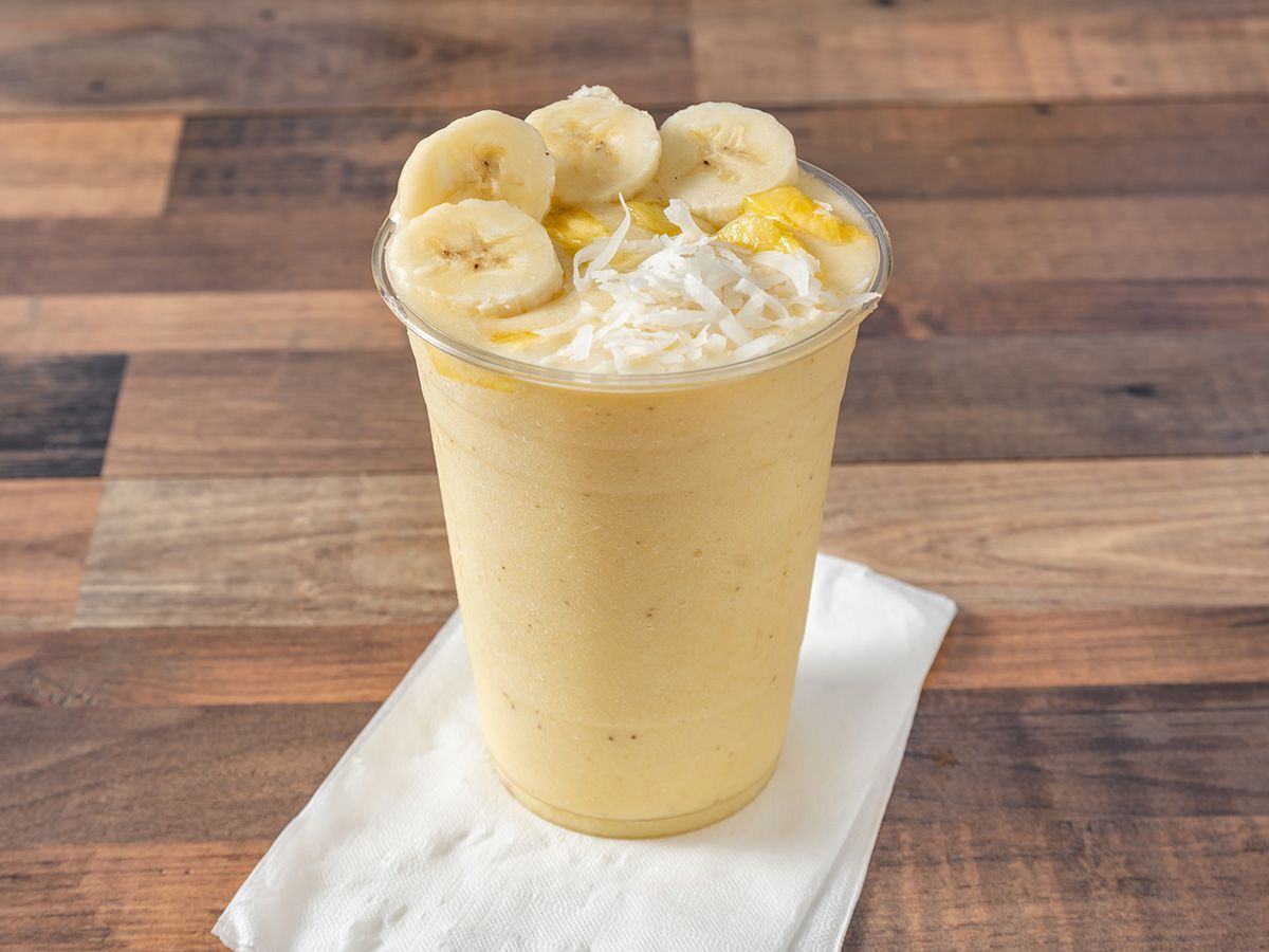 A banana smoothie in a plastic cup on a napkin on a wooden table.
