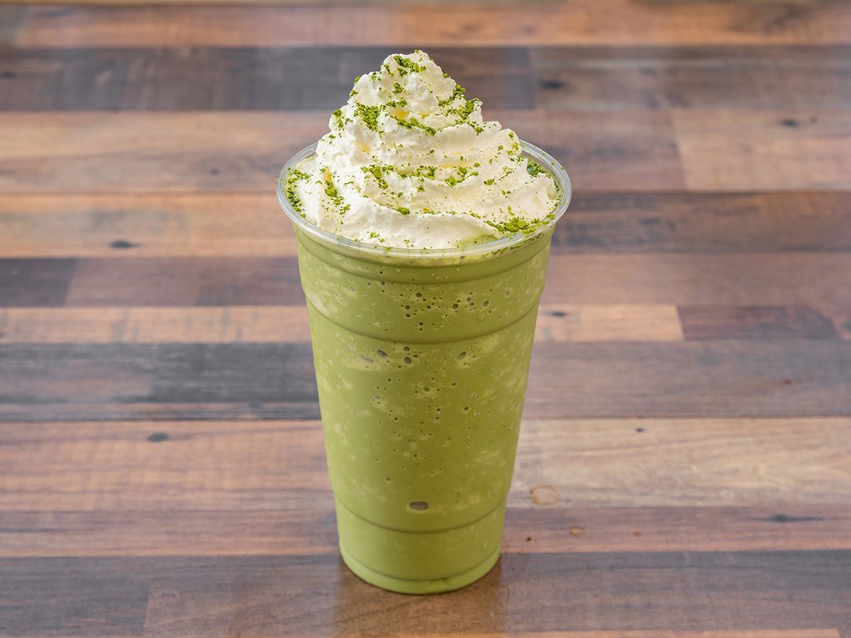 A green smoothie with whipped cream on top is on a wooden table.