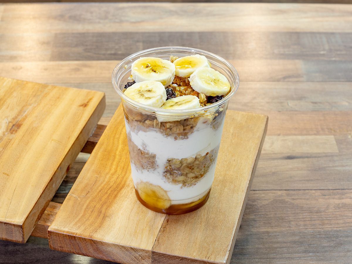 A cup of yogurt with bananas and granola on a wooden table.