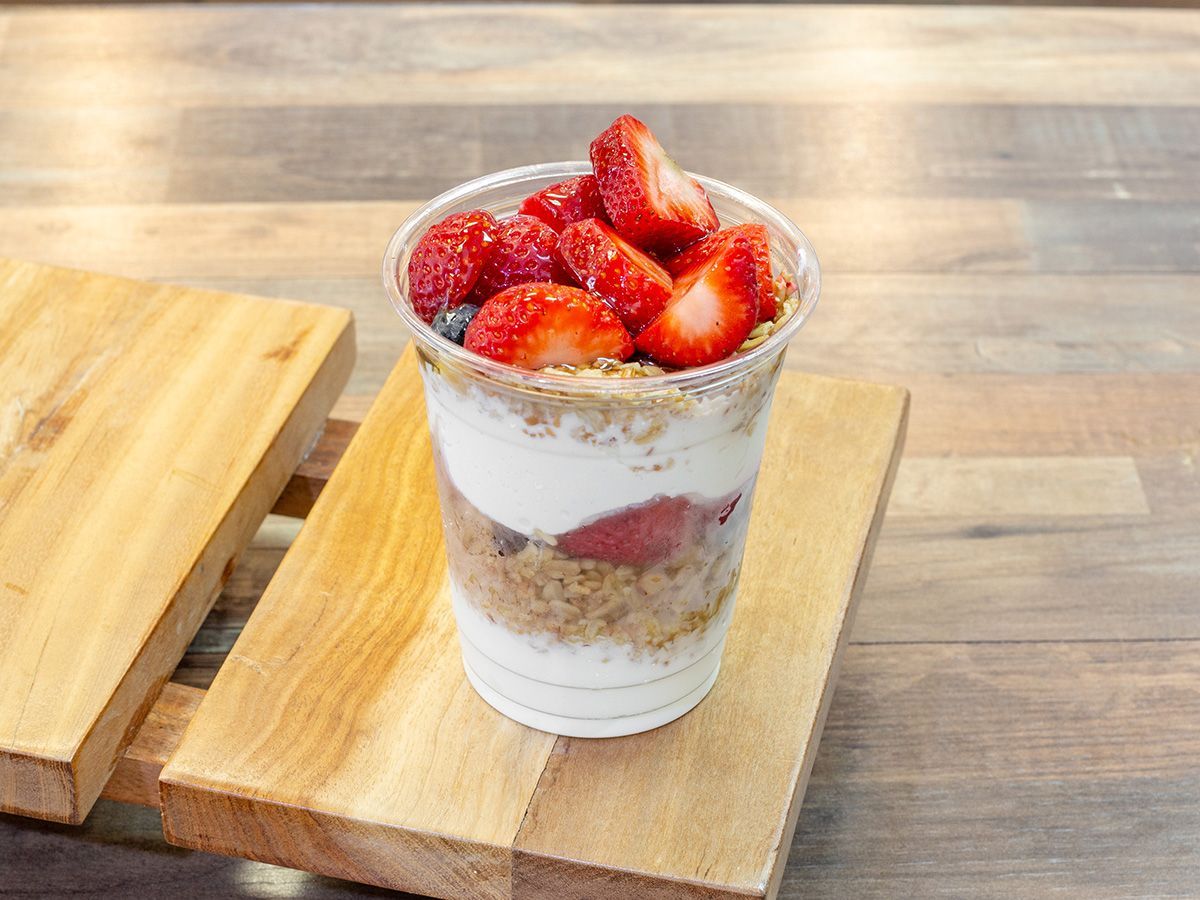 A cup of yogurt with strawberries and blueberries on a wooden cutting board.