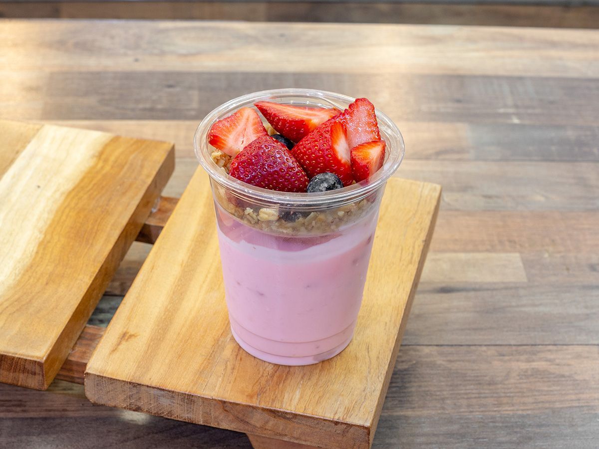 A cup of yogurt with strawberries and blueberries on a wooden table.
