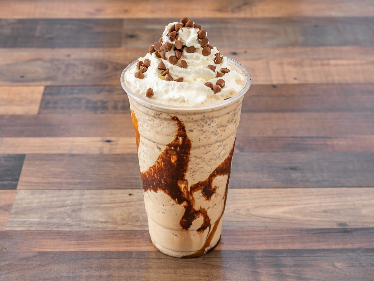 A milkshake with whipped cream and chocolate chips on top is on a wooden table.