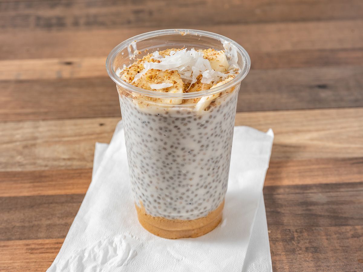 A glass of chia seed pudding with bananas and coconut on a napkin on a wooden table.