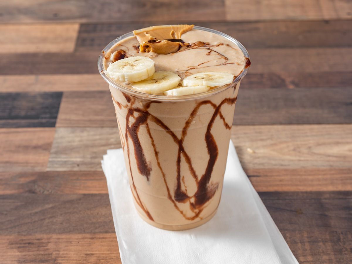 A milkshake with bananas , peanut butter and chocolate sauce on a wooden table.