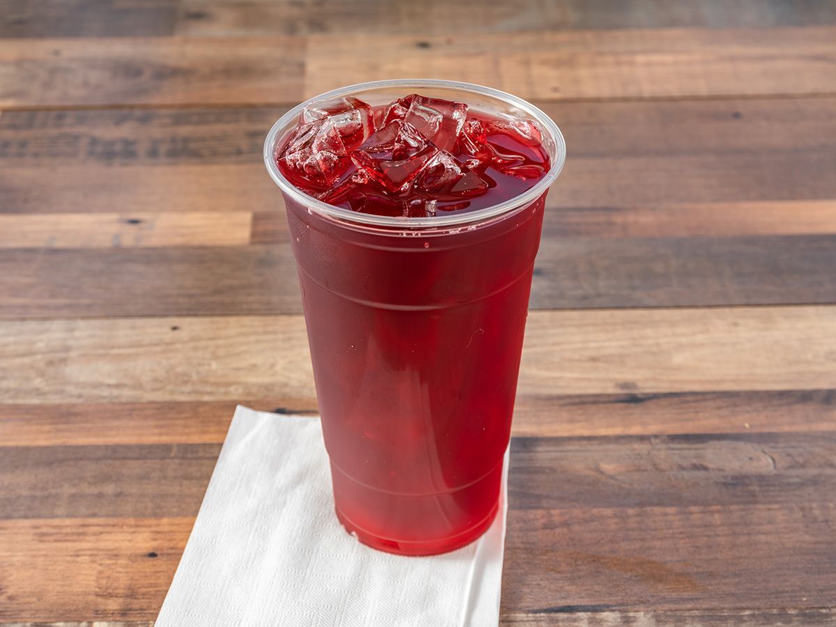 A plastic cup filled with red liquid is sitting on a napkin on a wooden table.
