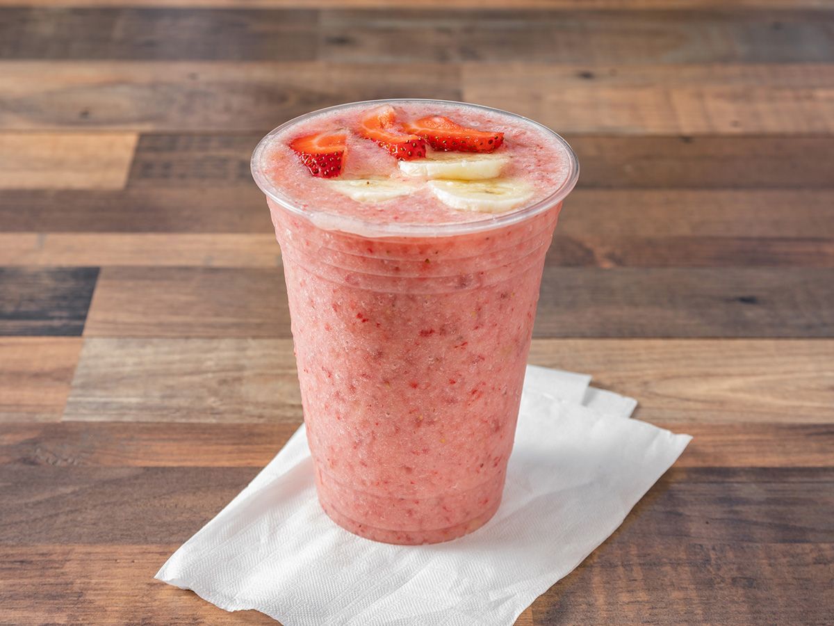 A pink smoothie with strawberries and bananas is on a napkin on a wooden table.