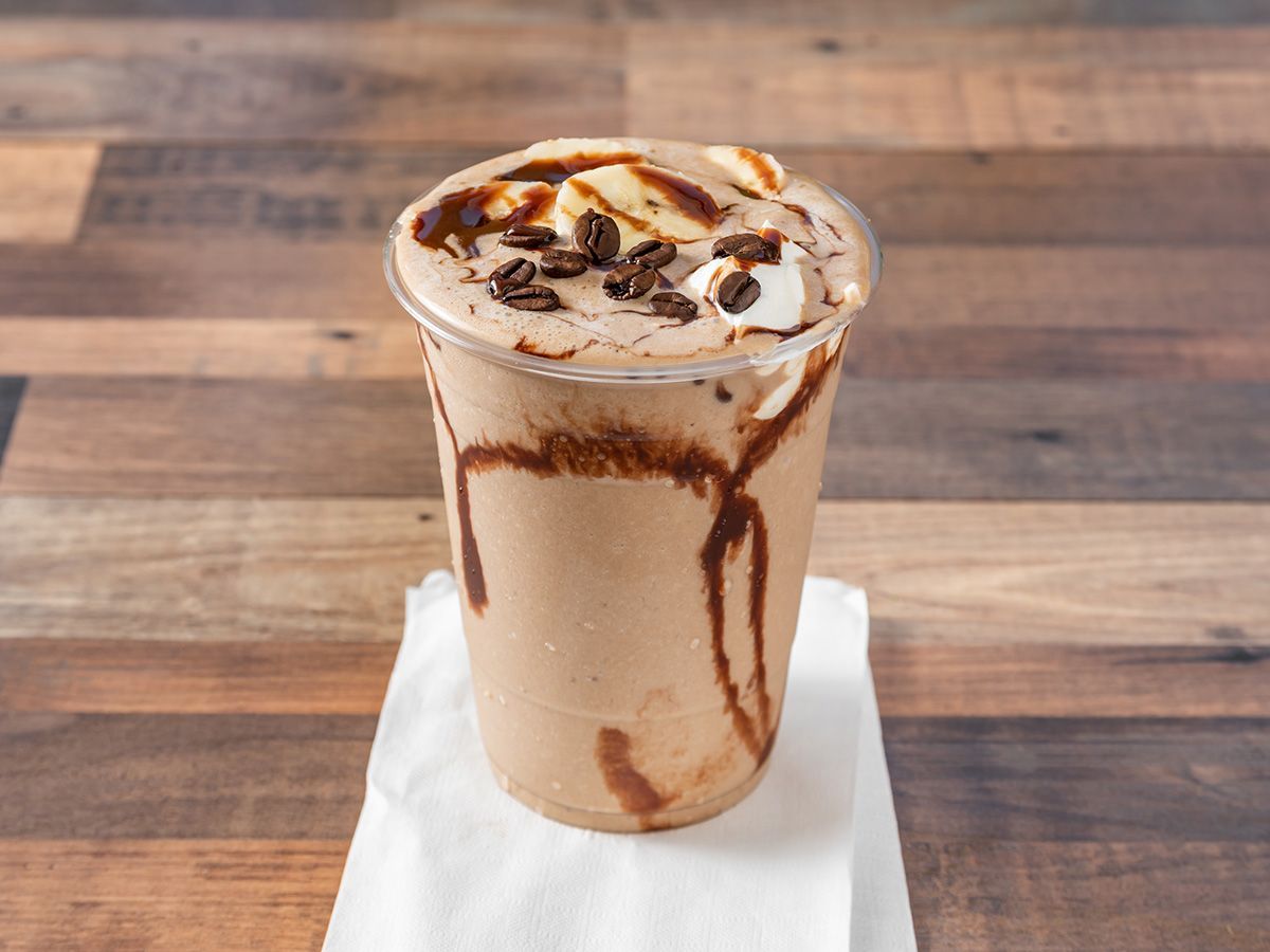 A milkshake with chocolate sauce and marshmallows is sitting on a napkin on a wooden table.