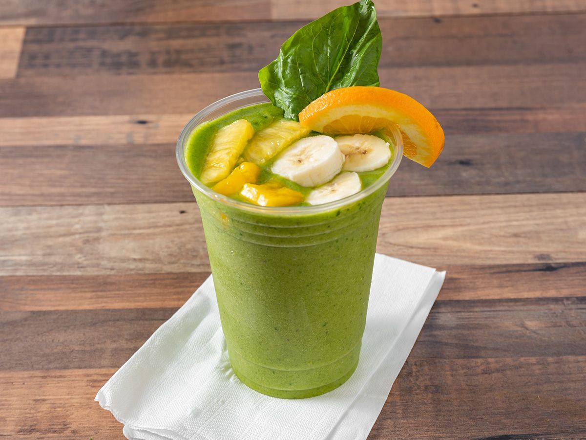 A green smoothie with bananas , pineapple and orange slices on a napkin on a wooden table.