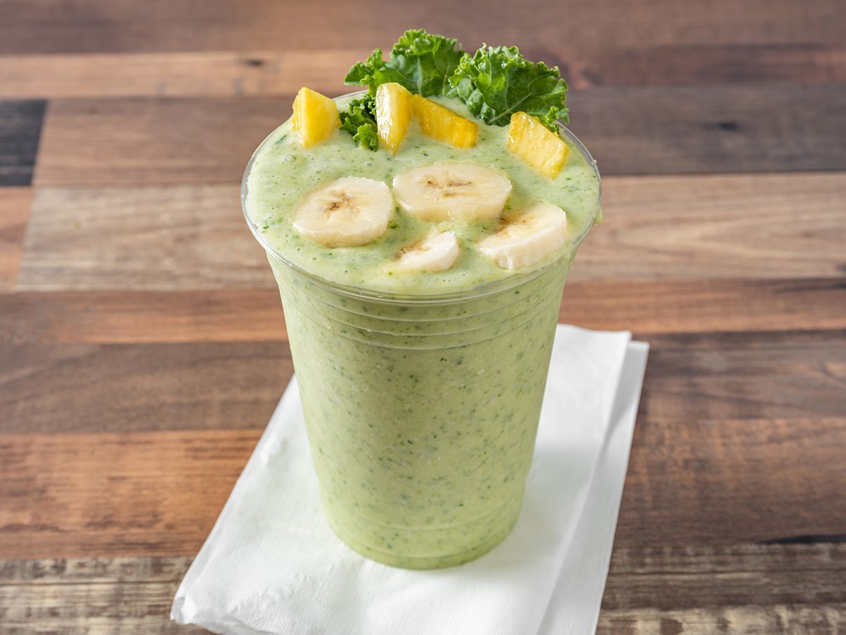 A green smoothie with bananas and lettuce in a cup on a napkin on a wooden table.