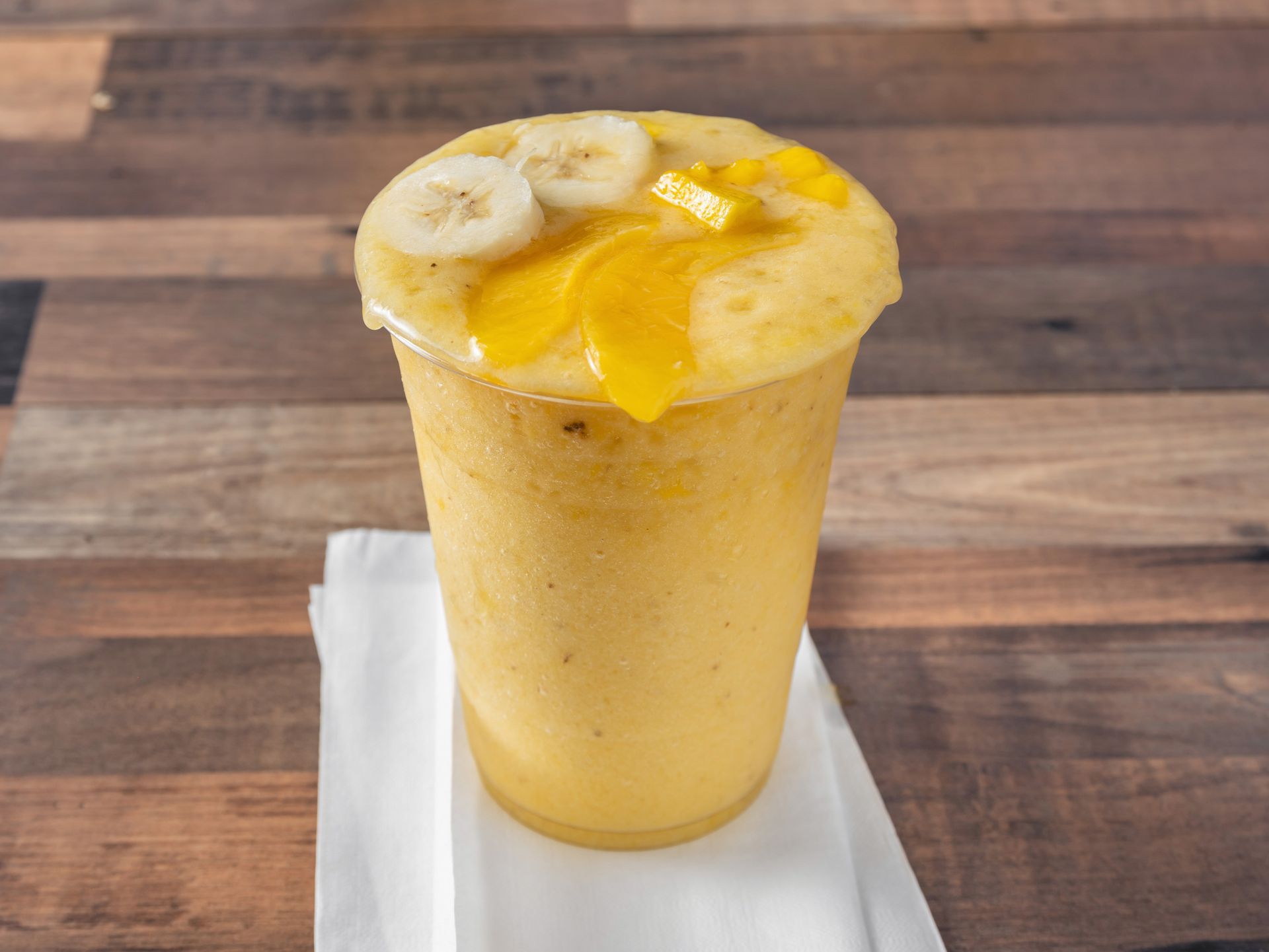 A yellow smoothie with bananas and mango slices on top