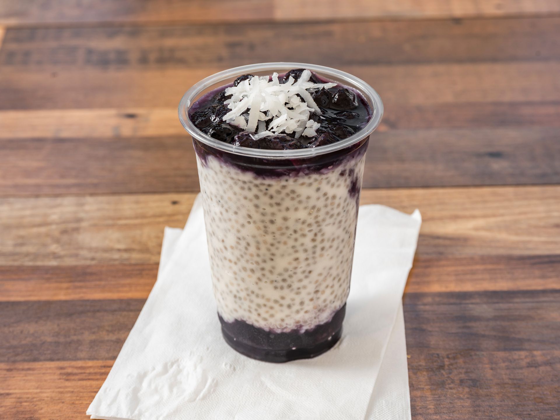 A drink in a plastic cup on a napkin on a wooden table.