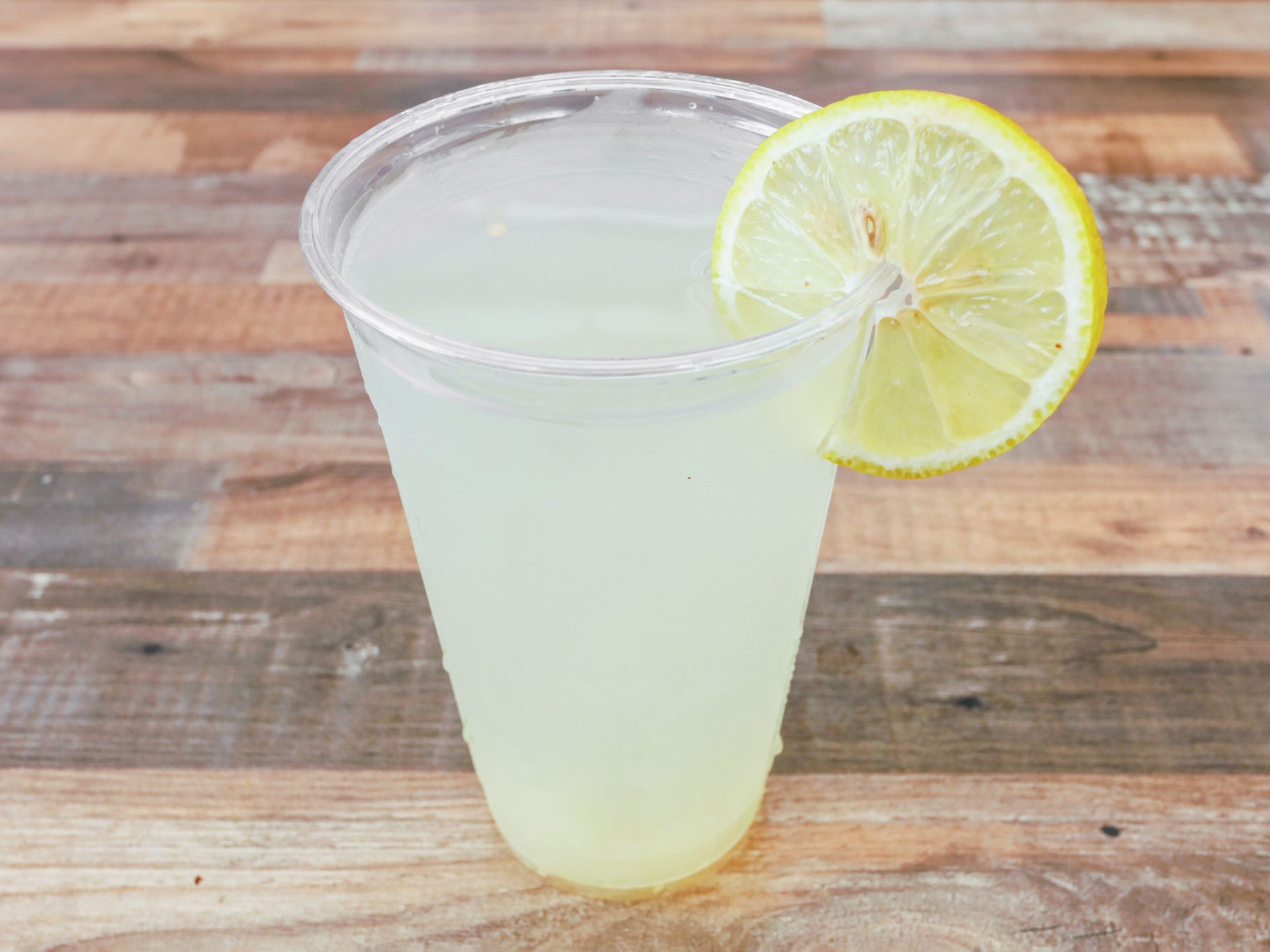 A cup of lemonade with a slice of lemon on a wooden table.