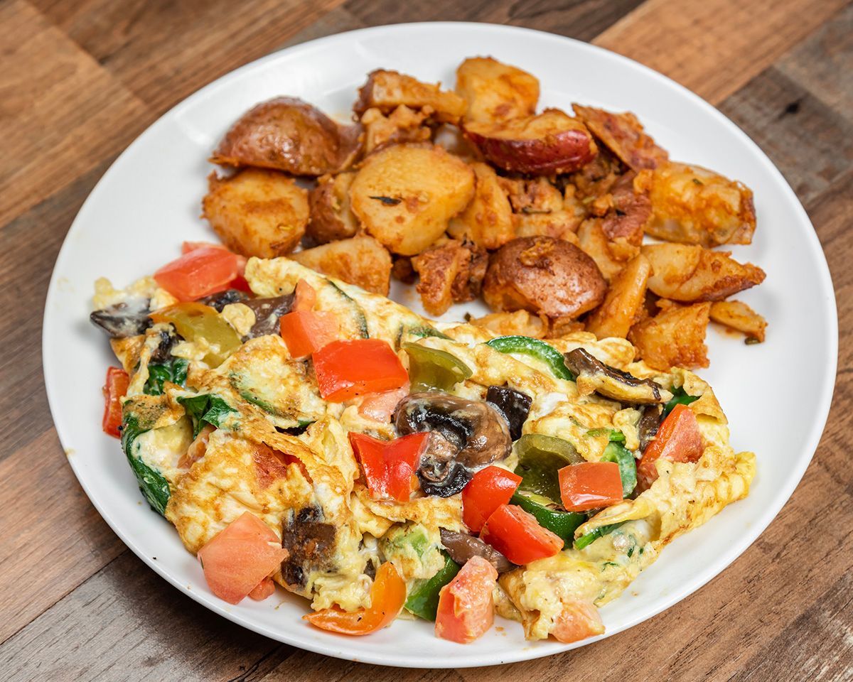 A plate of food with eggs, potatoes, and tomatoes on a wooden table.