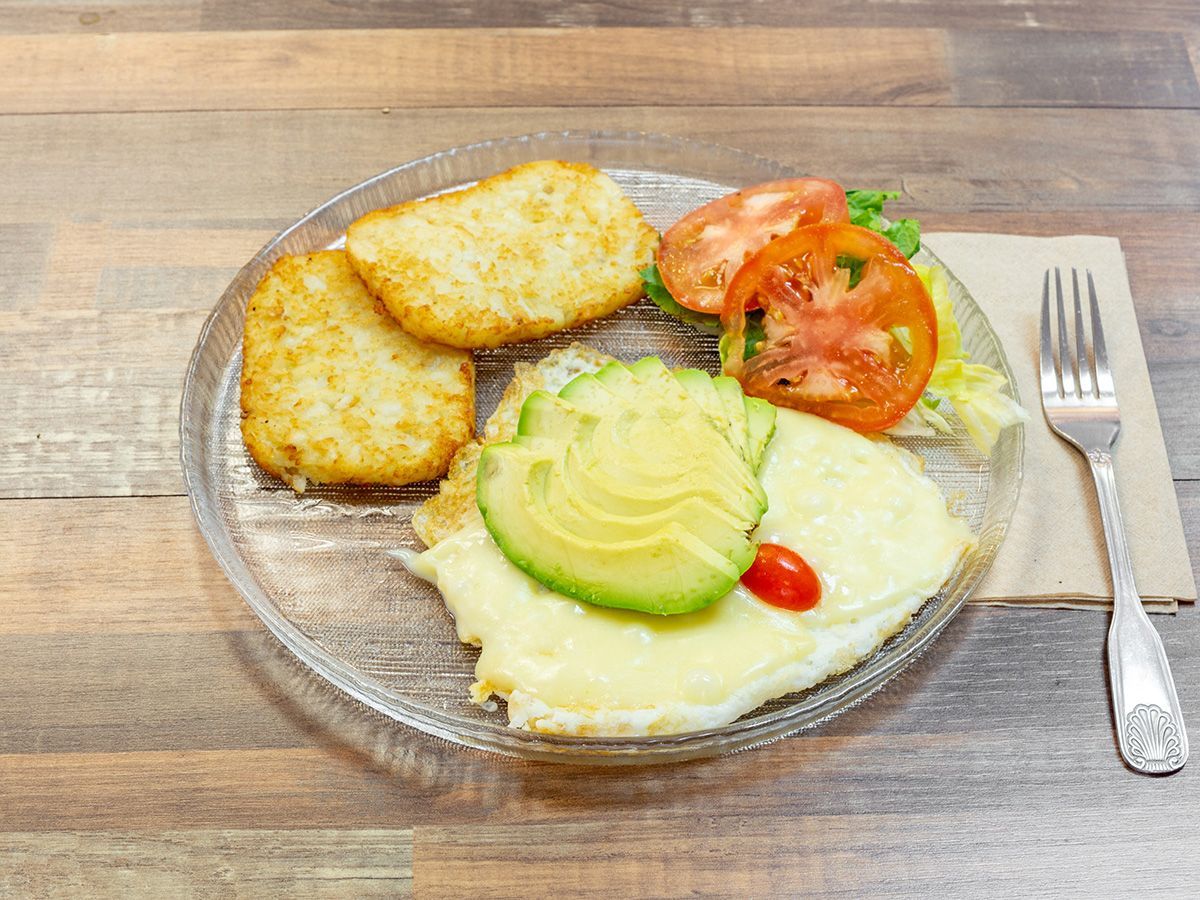 A plate of food with eggs , hash browns , avocado and tomatoes on a wooden table.
