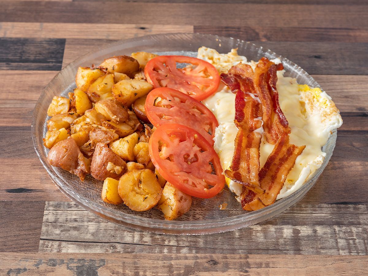 A plate of food with eggs, bacon, potatoes and tomatoes on a wooden table.