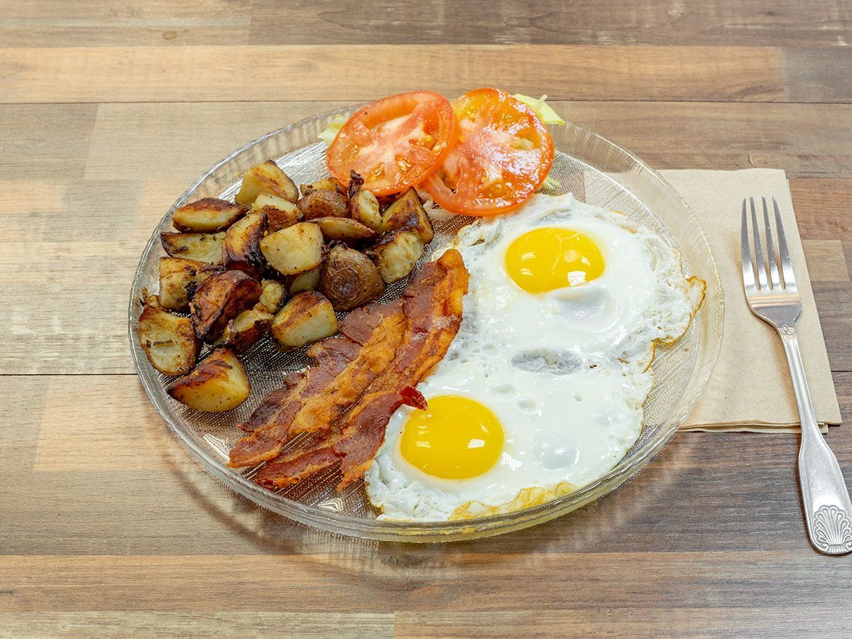A plate of food with eggs, bacon, potatoes and tomatoes on a wooden table.