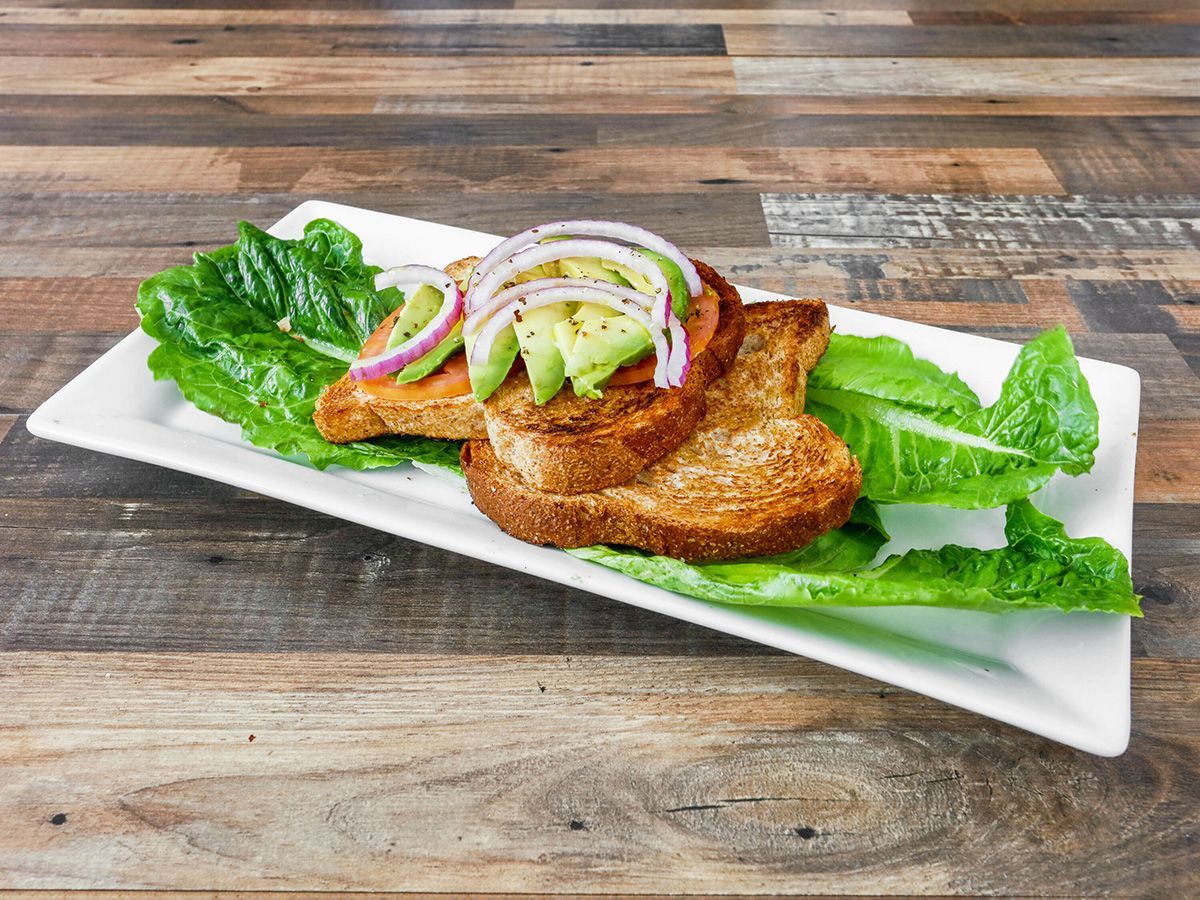 Two pieces of toast with avocado, lettuce and onions on a white plate on a wooden table.