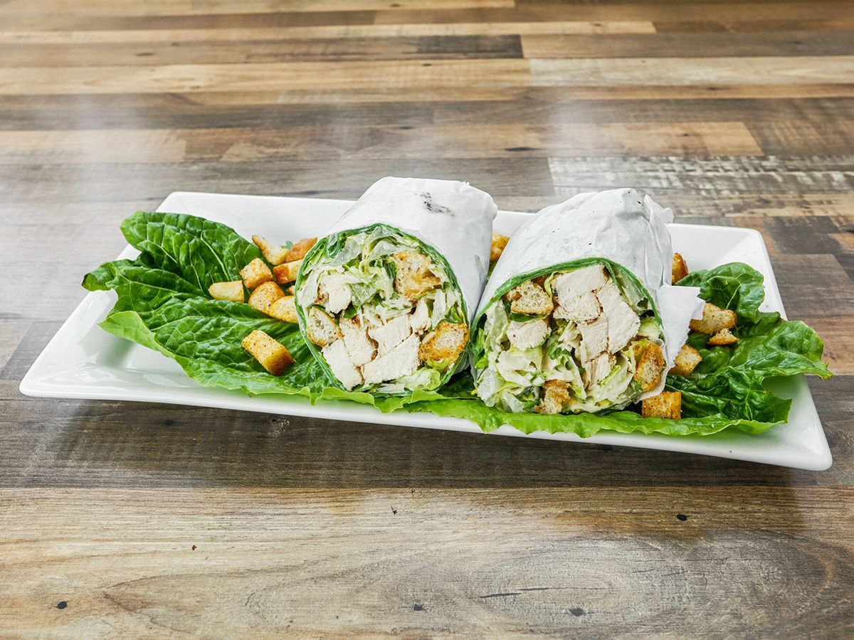 Two chicken caesar wraps on a white plate on a wooden table.