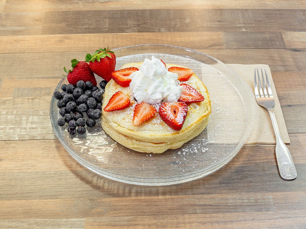 A plate of pancakes with whipped cream and strawberries on a wooden table.