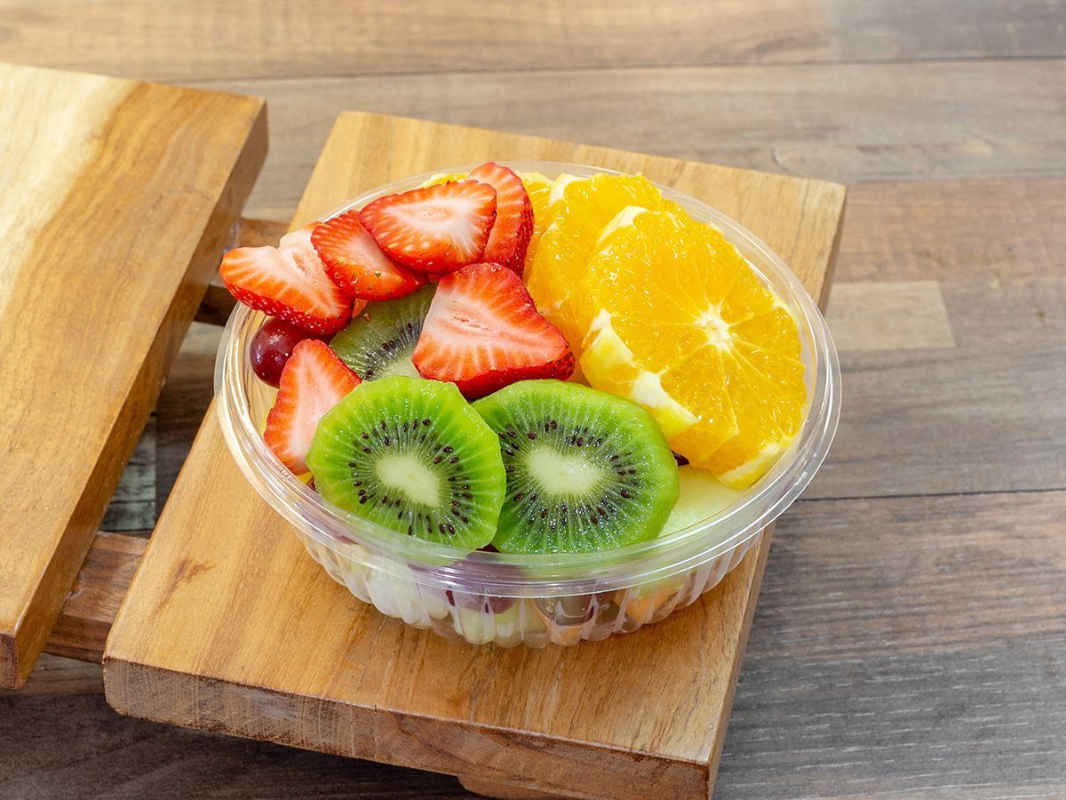 A bowl of fruit salad with strawberries, kiwi, and oranges on a wooden cutting board.