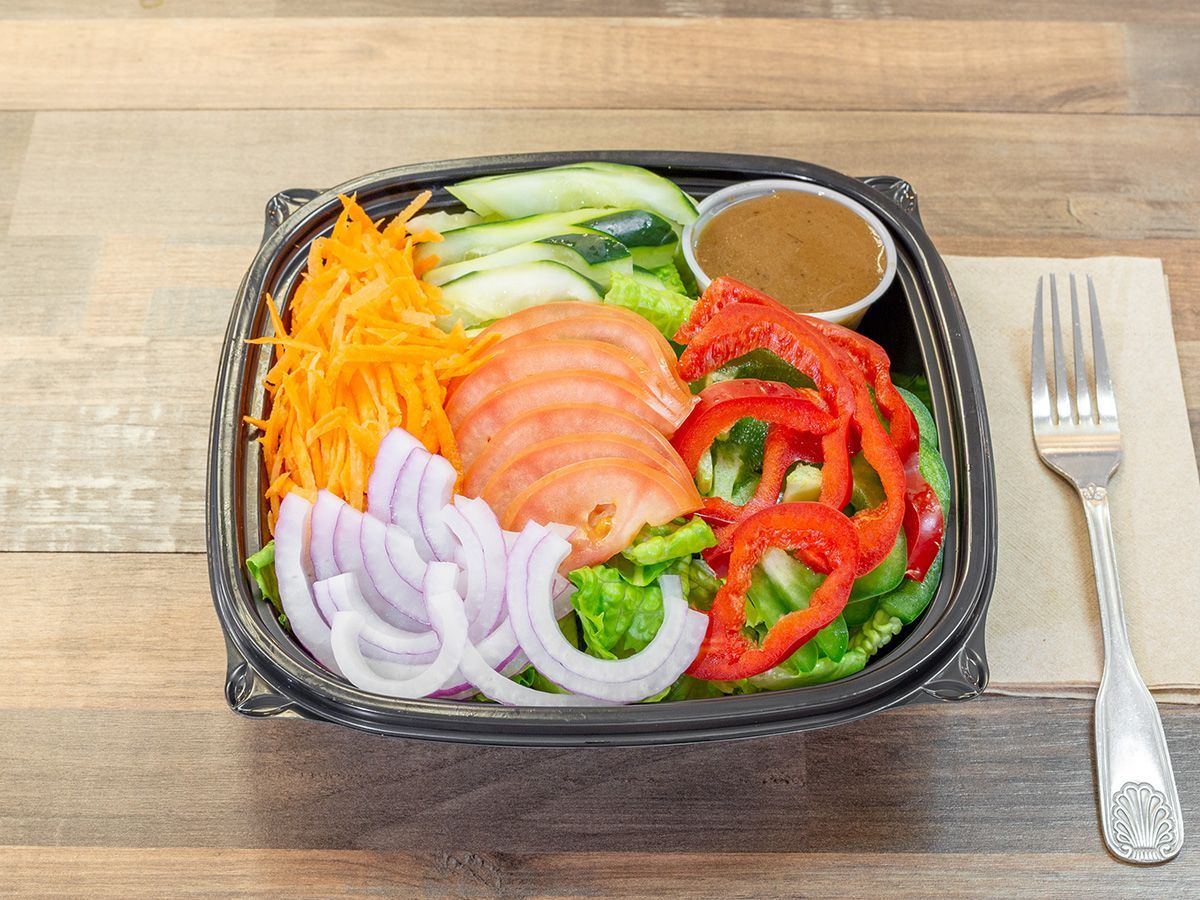 A salad in a plastic container with a fork on a wooden table.