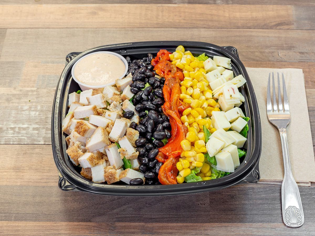 A salad in a plastic container with a fork on a wooden table.