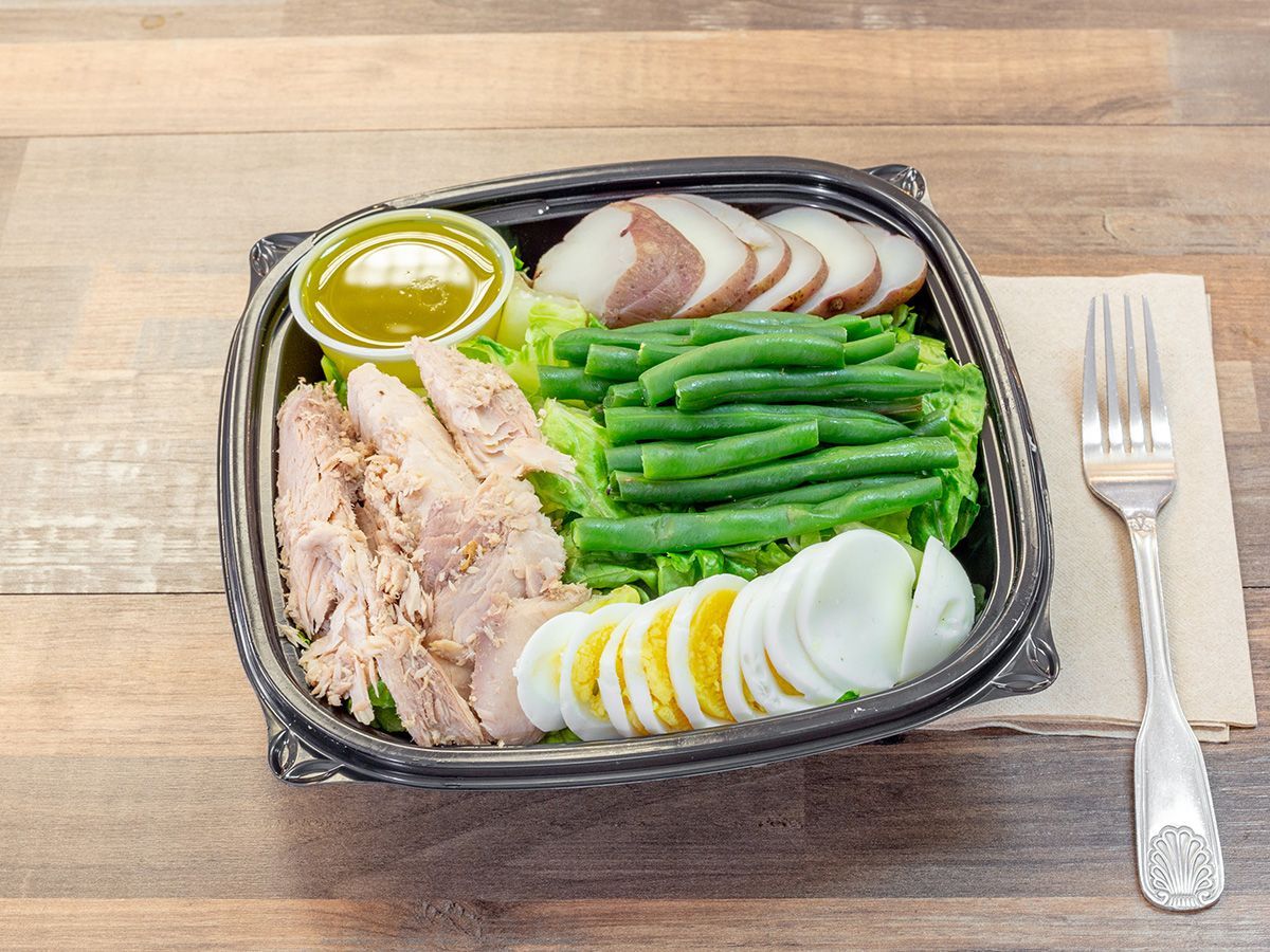 A salad in a plastic container on a wooden table with a fork and napkin.