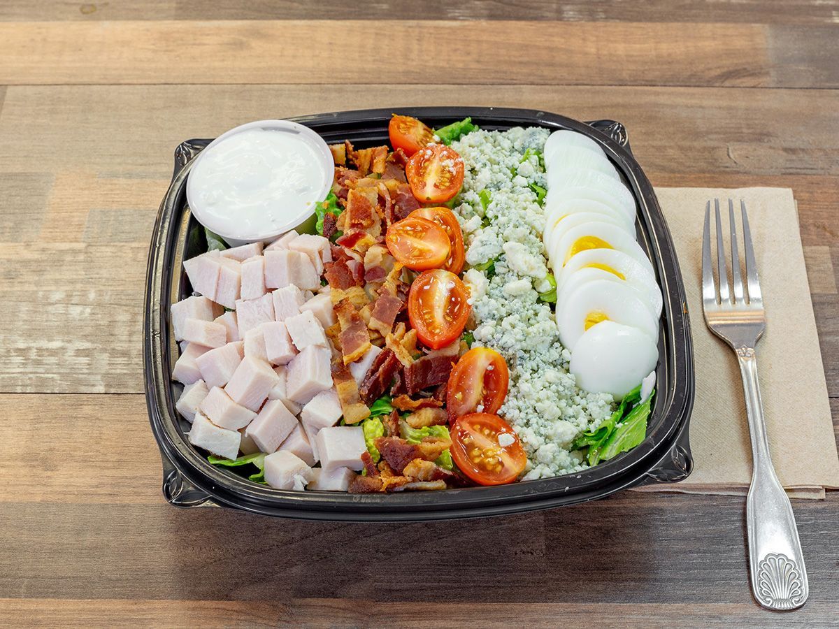 A salad in a plastic container with a fork on a wooden table.