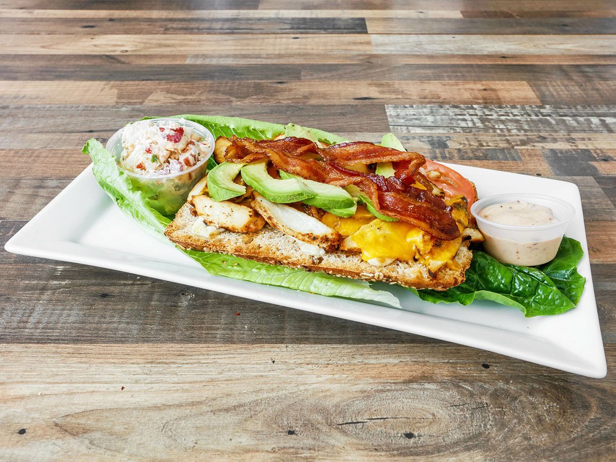 A sandwich with avocado, bacon, cheese and lettuce on a white plate on a wooden table.