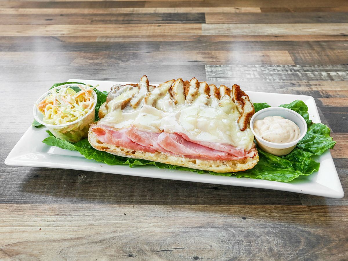 A white plate topped with a sandwich and coleslaw on a wooden table.