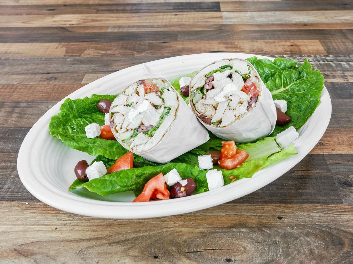 A white plate topped with two wraps and a salad on a wooden table.