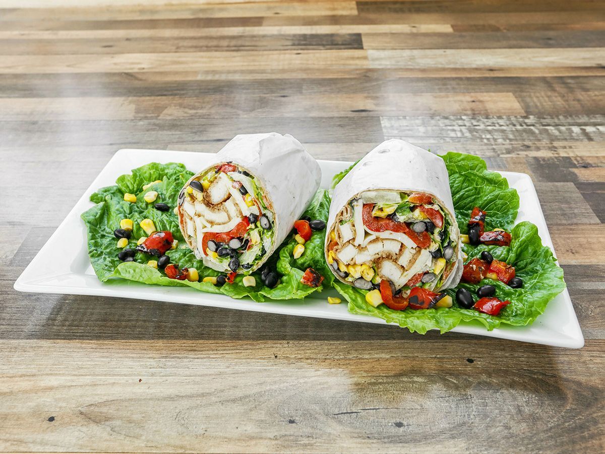 Two burritos are sitting on a white plate on a wooden table.
