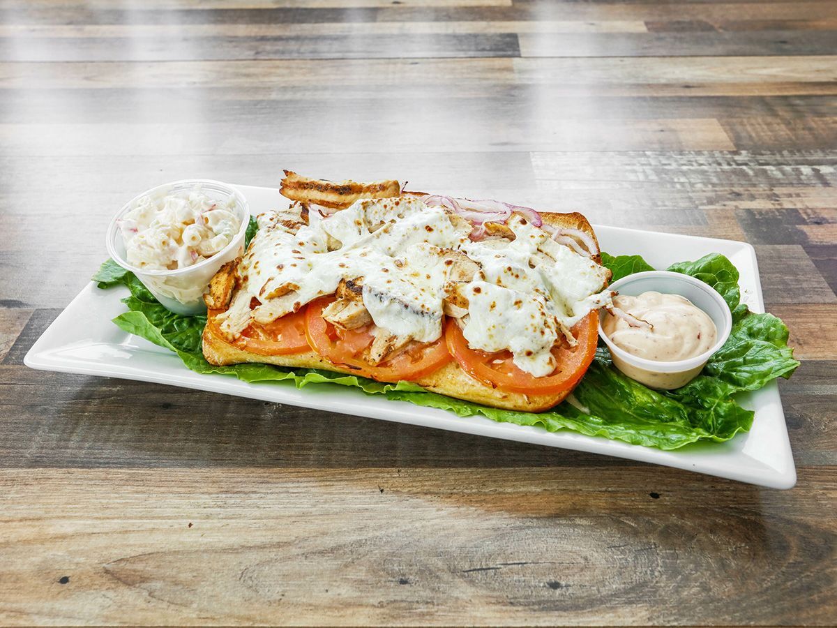 A sandwich with tomatoes, cheese and lettuce on a white plate on a wooden table.