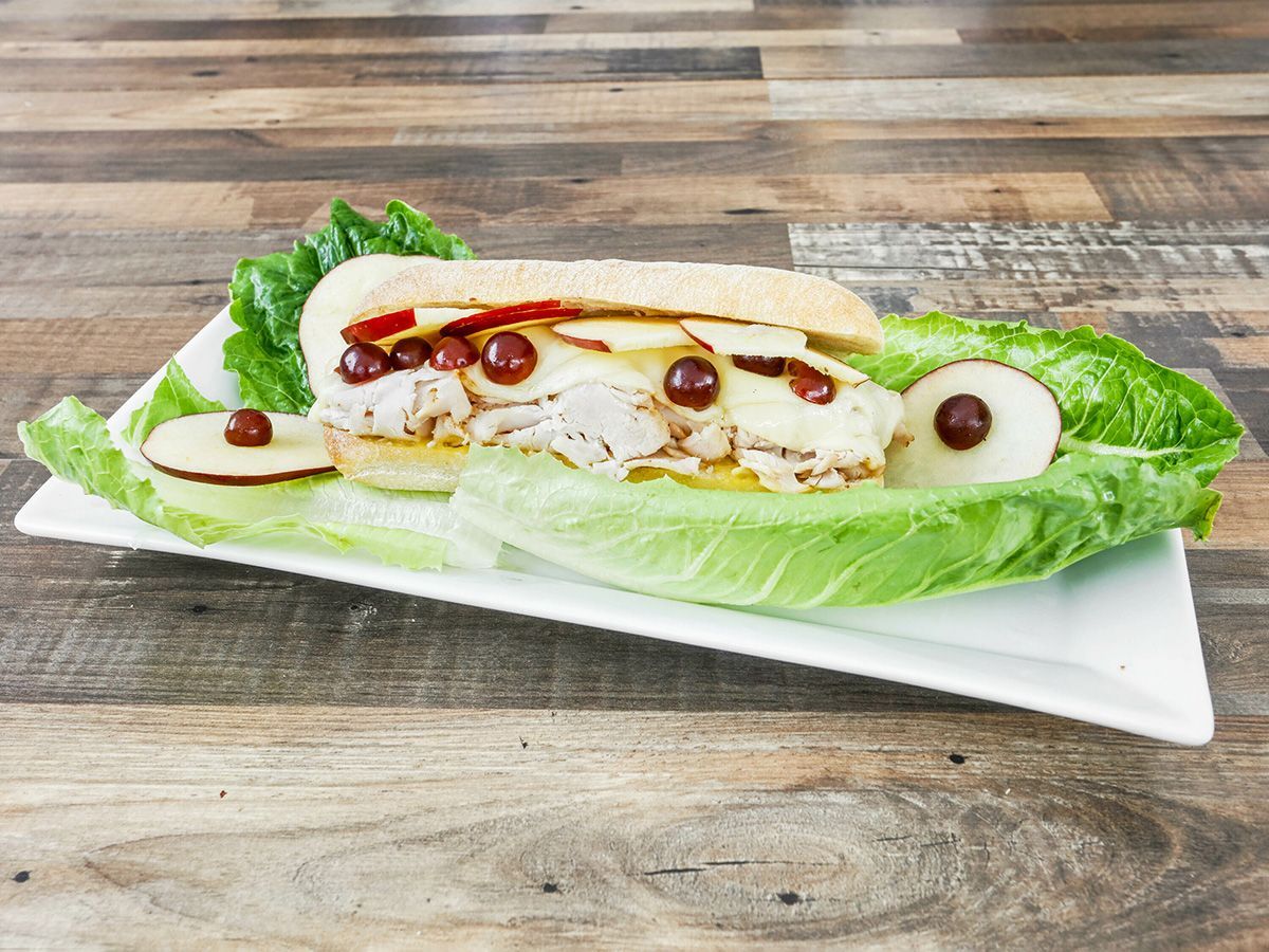 A sandwich on a lettuce leaf on a white plate on a wooden table.