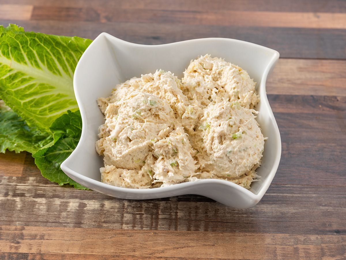 A bowl of chicken salad is sitting on a wooden table next to lettuce.