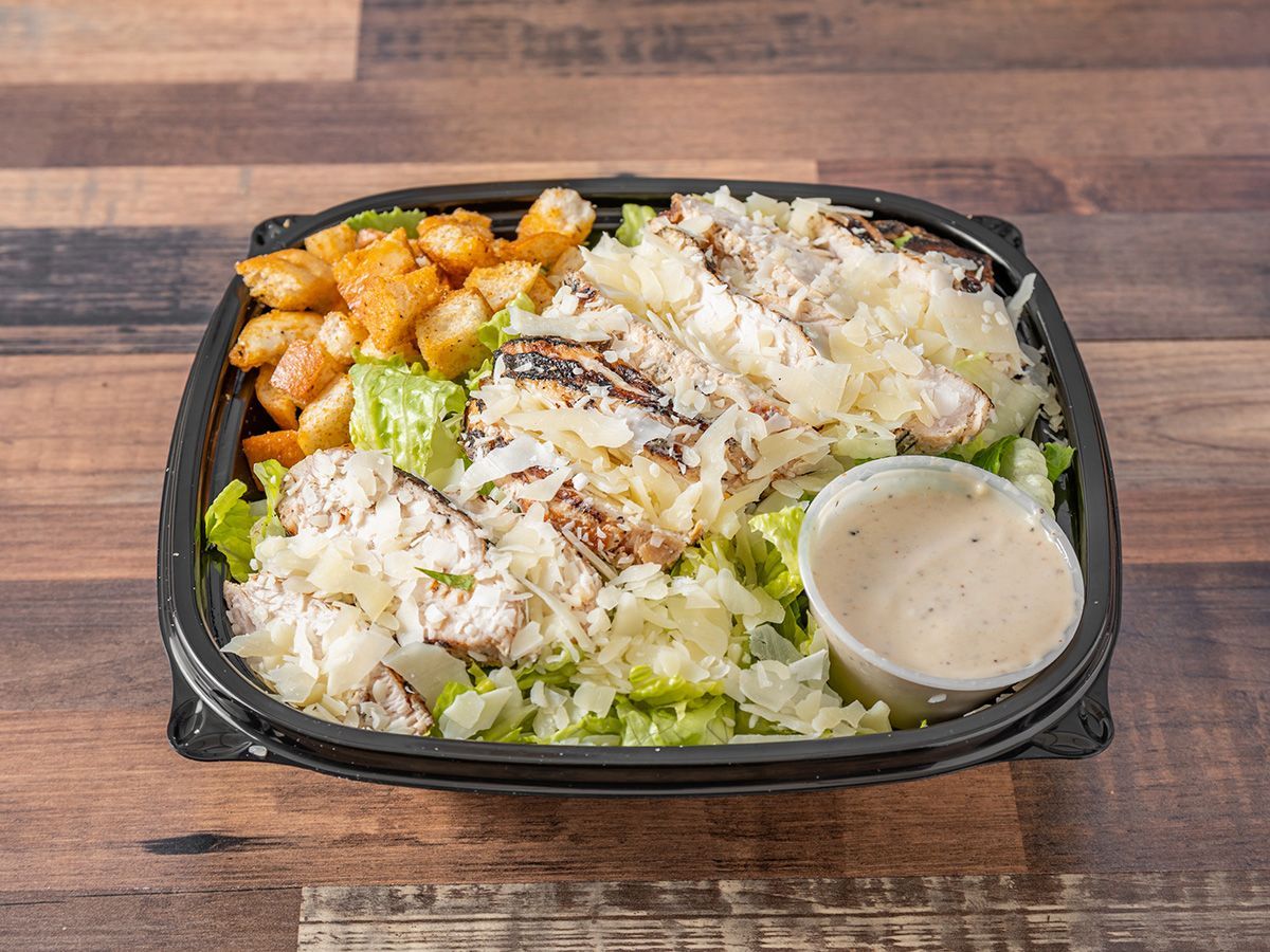 A caesar salad in a plastic container on a wooden table.