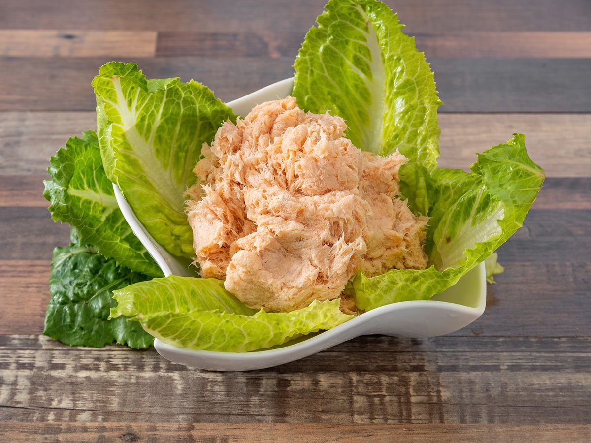 A bowl of tuna salad on lettuce leaves on a wooden table.