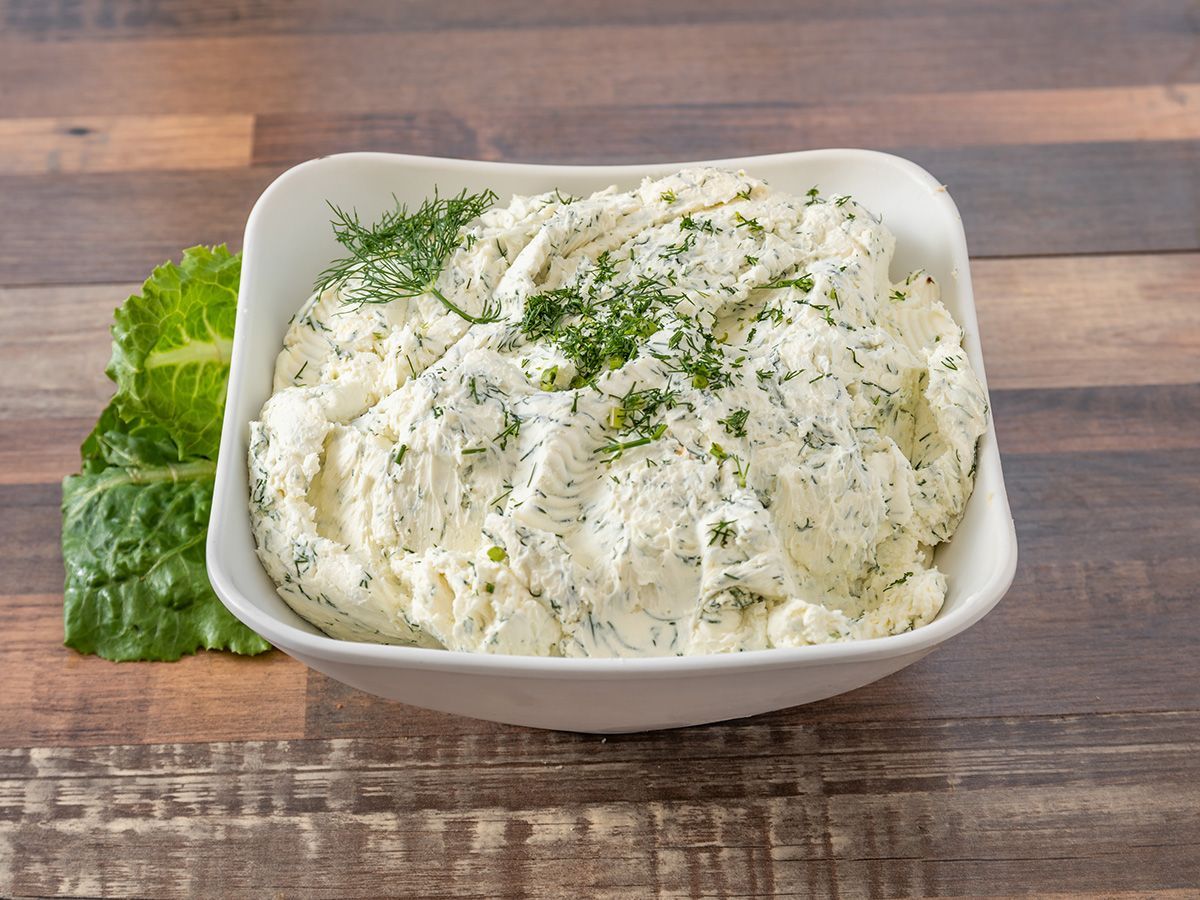 A bowl of mashed potatoes with dill on a wooden table.